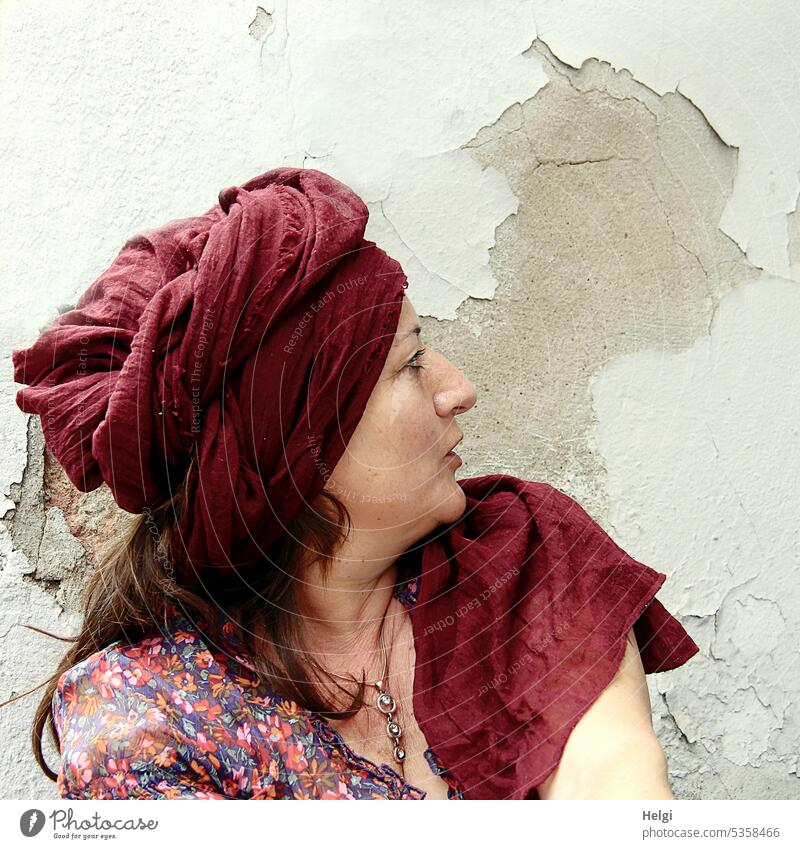 Gegenüberstellung | langhaarige brünette Frau mit Turban schaut zur Wand, auf der durch abgeblätterte Farbe ein Kopf dargestellt  ist Porträt Profil Figur Bluse