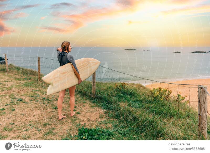 Surferin, die ihr Haar hochsteckt, während sie vom Ufer aus auf den Strand blickt Frau jung Setzen Haare aufstellen Blick Surfbrett Sonnenuntergang Sonnenlicht