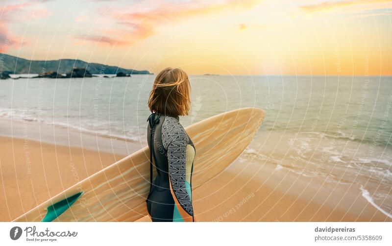 Surferin mit Neoprenanzug und Surfbrett am Strand mit Blick auf das Meer unkenntlich jung Frau Sonnenuntergang Sonnenlicht Horizont MEER Küste Sand Sommer