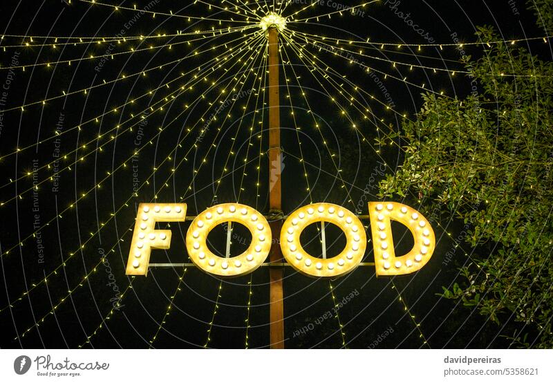 Schild mit dem Wort Essen aus Glühbirnen an einem Holzpfosten unter Lichtergirlanden aufgehängt signalisieren Lebensmittel Zeichen Beleuchtung Knolle Girlande