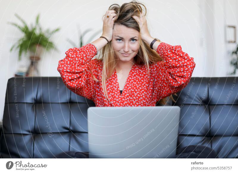 Blonde Frau sitzt auf dem Sofa und dem Laptop, die Hände auf dem Kopf und schaut in die Kamera blond Sitzen in die Kamera schauen Stress Frustration müde