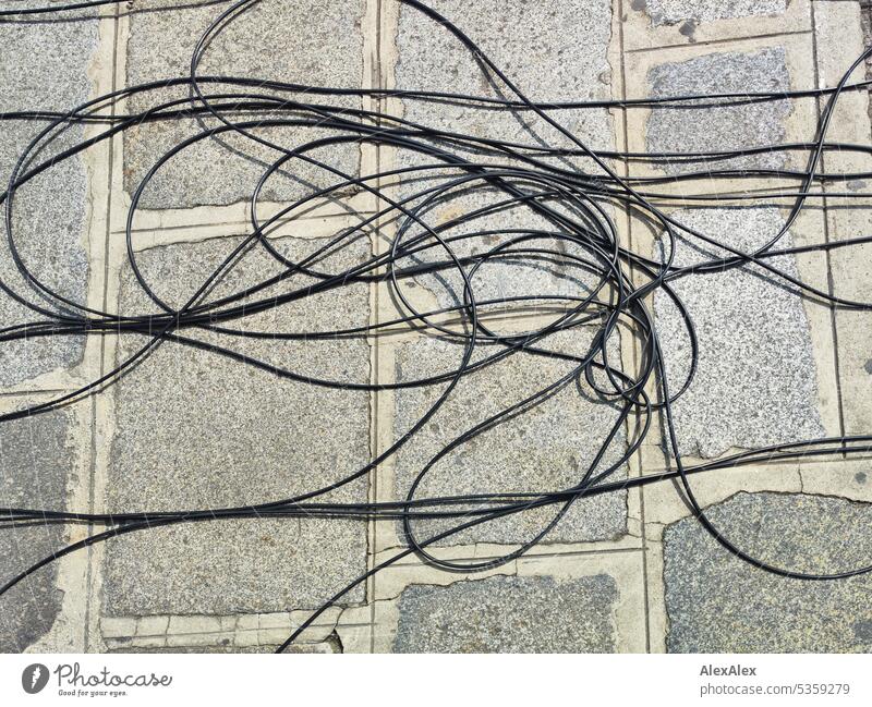Schwarzes, langes Kabel auf dem Gehweg, mäßig verheddert Boden Stromleitung Energie sparen Energiekrise Stromtransport Leitung Energiewirtschaft