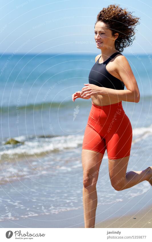 Lächelnde Sportlerin läuft am Sandstrand in der Nähe von Meerwasser Frau Strand MEER Training joggen Fitness Barfuß Sommer jung Glück Energie Aktivität