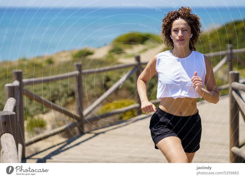 Fitte Frau beim Joggen auf einem Holzsteg an einem sonnigen Tag Sportlerin joggen laufen Training Gesundheit Übung Vitalität passen selbstbewusst Strand