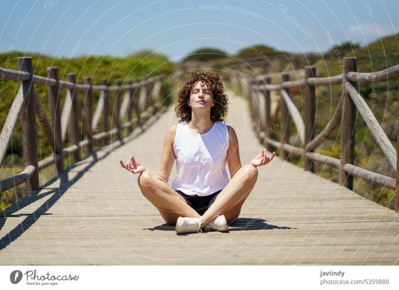 Entspannte junge Frau beim Meditieren auf einem Holzpfad meditieren Yoga üben Lotus-Pose Zen Natur padmasana Asana Windstille friedlich sich[Akk] entspannen