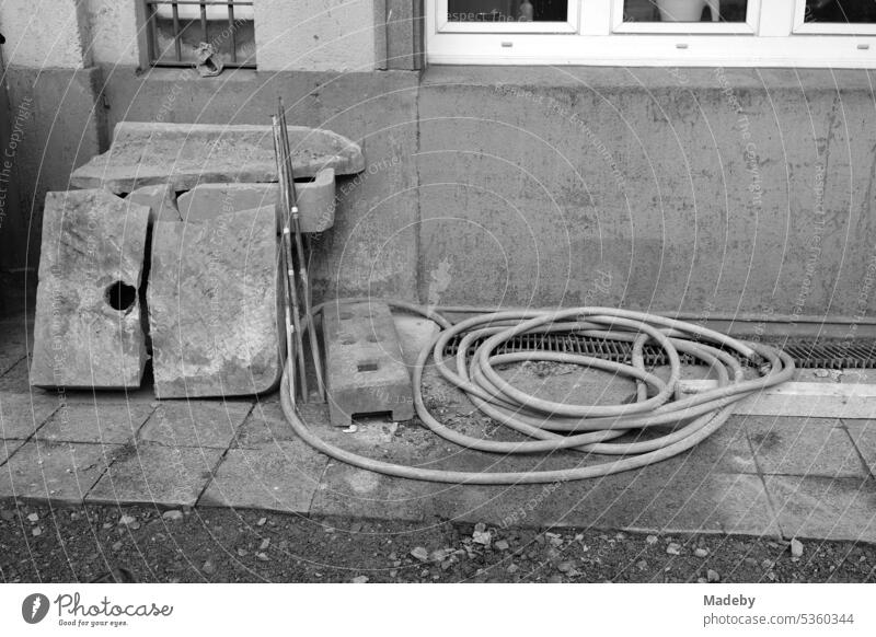 Gartenschlauch neben alten grauen Steinen in einem heruntergekommenen Hinterhof der gentrifzierten Braubachstraße in der Altstadt von Frankfurt am Main in Hessen in neorealistischem Schwarzweiß