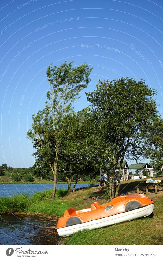 Altes Tretboot aus Kunststoff in Orange am Ufer und am Bootssteg im Sommer vor blauem Himmel im Sonnenschein am Poyrazlar Gölü bei Adapazari in der Provinz Sakarya in der Türkei