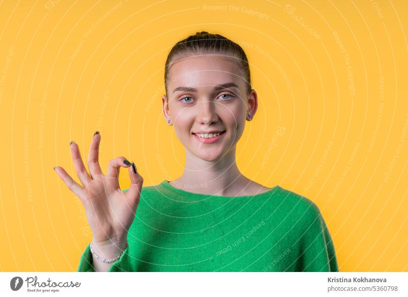 Hübsche Frau mit OKAY-Zeichen, ok-Geste. Glückliche Dame, richtige Wahl auf Gelb gestikulieren gut okay ja Vereinbarung Hand Befriedigung Symbol genehmigen