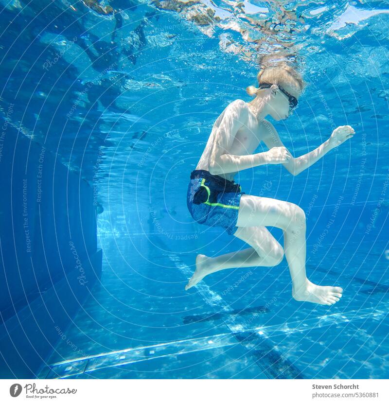 Blonder Junge macht eine Rolle unter blauem Wasser im Schwimmbad blond blondes Haar blonder Junge unter Wasser Unterwasseraufnahme Pool warm warmes Wetter