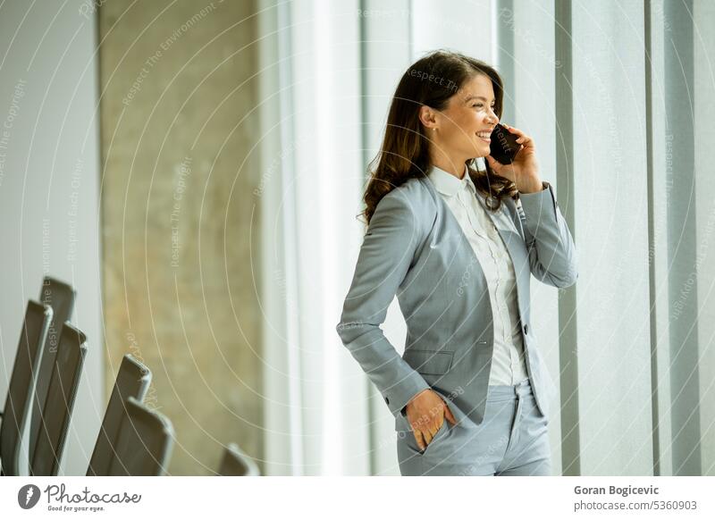 Junge Frau, die ein Mobiltelefon am Bürofenster benutzt Erwachsener allein attraktiv schön Schönheit hell brünett Business Geschäftsperson Geschäftsleute