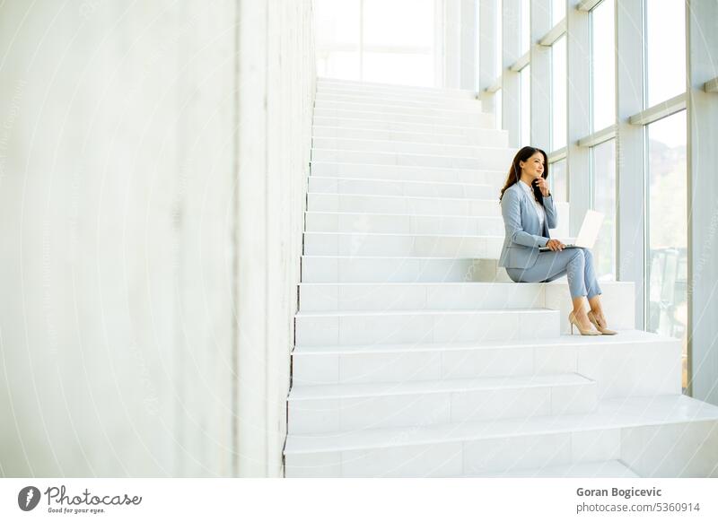 Junge Geschäftsfrau sitzt auf der Treppe im Büroflur und arbeitet am Laptop Internet modern Business Technik & Technologie Menschen Glück schön Mitteilung Frau