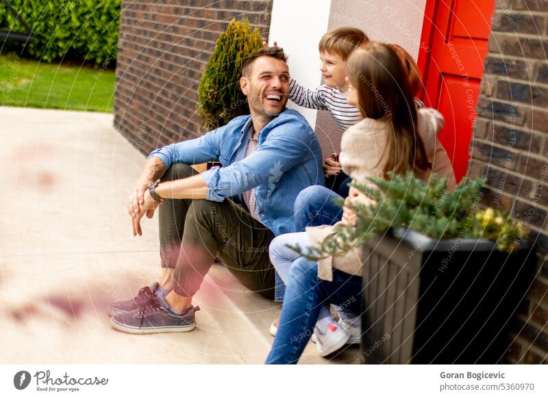 Familie mit Mutter, Vater, Sohn und Tochter sitzen draußen auf den Stufen einer Veranda eines Backsteinhauses Eltern Treppe Mädchen Kind Fröhlichkeit Kindheit