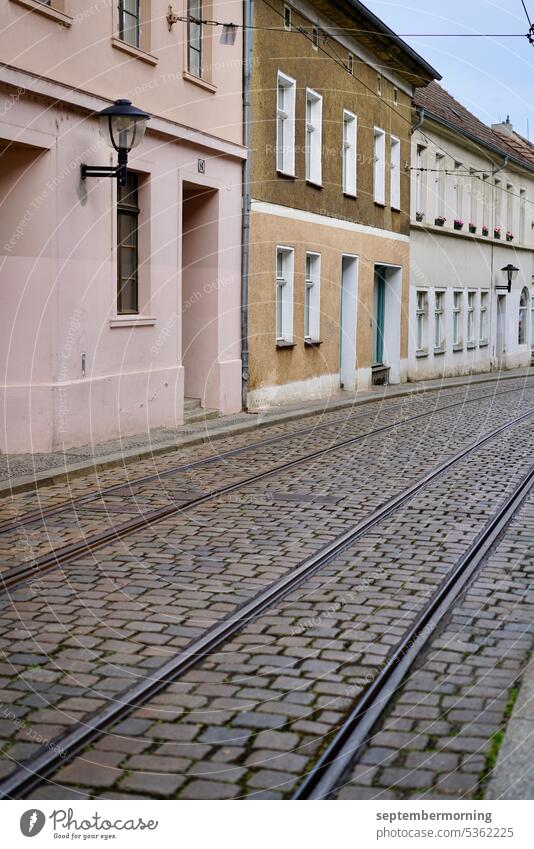 Kopfsteinstraße mit Straßenbahnschienen Menschenleer alte einstöckige Häuser Pastellfarben Kopfsteinpflaster bedeckter Himmel