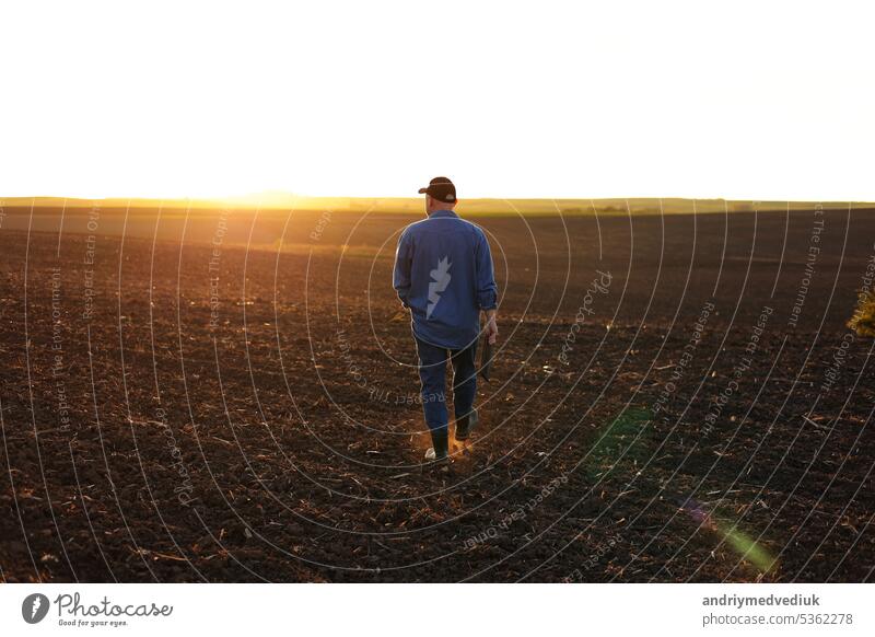 Agrarwirtschaft. Rückansicht eines männlichen Landwirts, der bei Sonnenuntergang im Frühling durch ein gepflügtes Feld geht. Besitzer landwirtschaftlichen Betrieb ist die Überprüfung und Prüfung Ackerland vor der Aussaat Landwirtschaft Pflanzen.