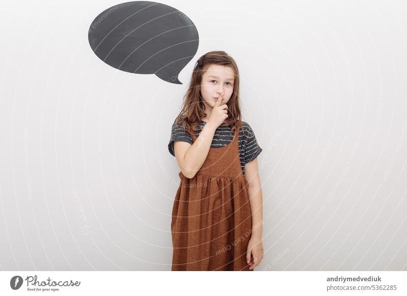 Ein kleines Mädchen hält den Zeigefinger in die Nähe des Mundes und zeigt damit eine Geste des Schweigens. Isoliert auf weißem Hintergrund. Pst. Geheimnis. Selektiver Fokus