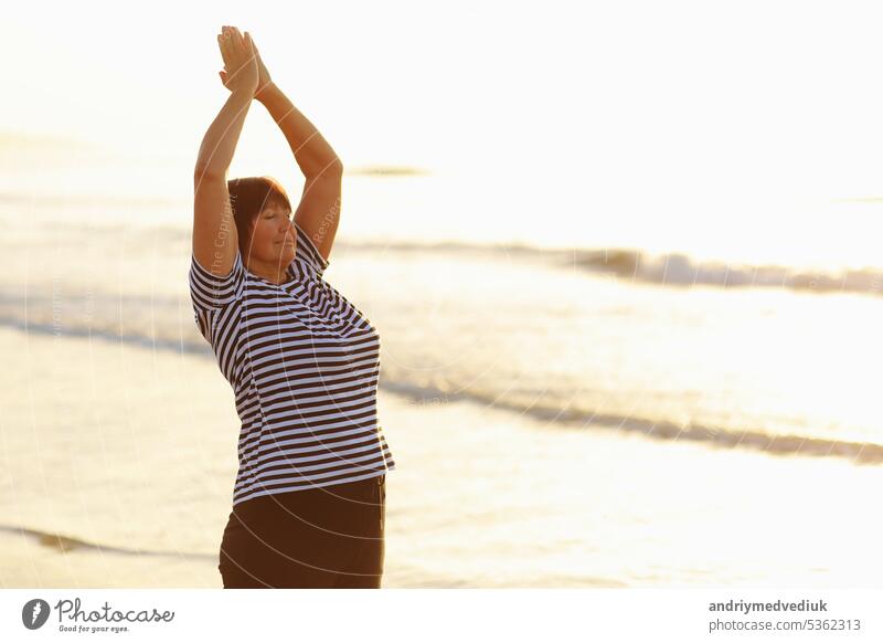 Yoga und Meditation der reifen Frau übt Atemübungen auf dem Meer Strand auf Sonnenaufgang am Morgen. Körper, Geist und Seele, Achtsamkeit Konzept. Erleuchtung und gesunden Lebensstil.
