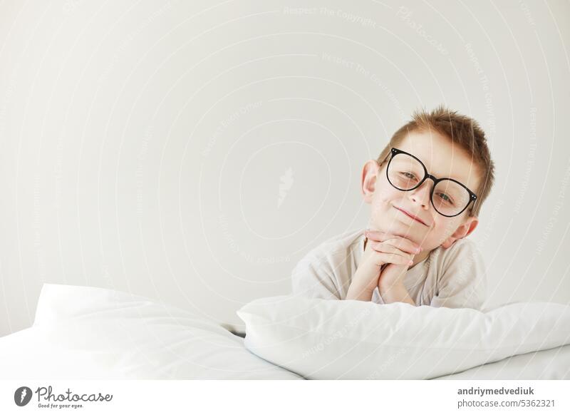 Adorable lächelnde Kind Junge mit Brille liegt im Bett. Morgen träumt auf weißen Bett. Kindheit schlafen Schlafzimmer Baby Mode Hand Liebe Person Buch Schule
