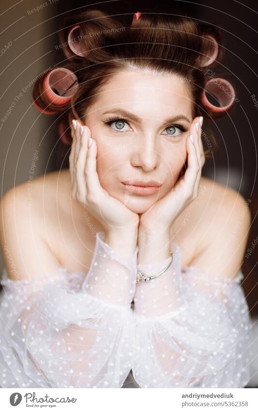 Eine schöne junge auffällige brünette Frau mit leuchtendem Pin-up-Make-up im langen weißen Spitzenkleid und rosa Lockenwicklern. Schönheitskonzept. internationaler Frauentag