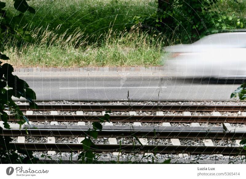 Gleise und Straße, eine graue Limousine ist mit hoher Geschwindigkeit unterwegs... Bahn Stadtbahn Verkehr Schienenverkehr fahren Gleisbett Sommer sommerlich