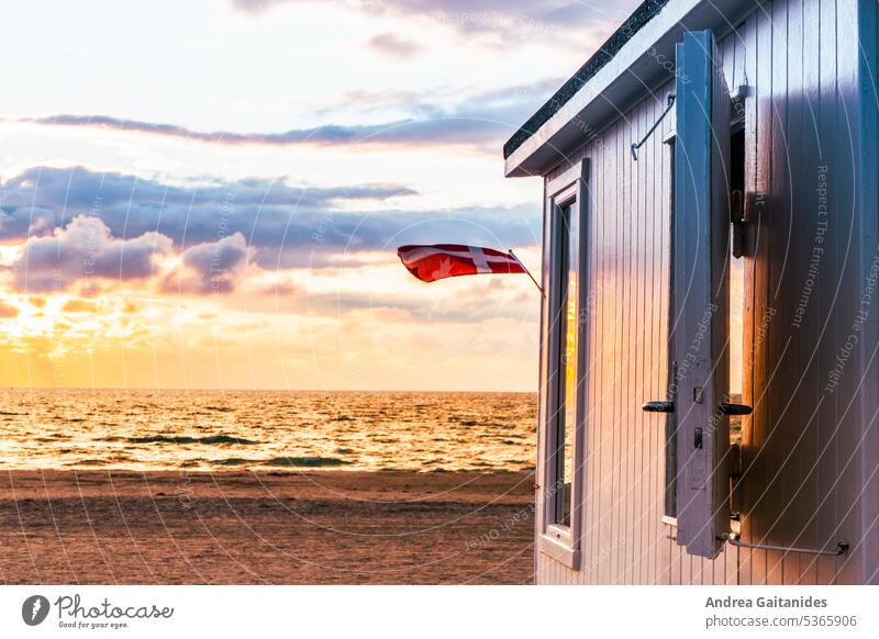 Teilansicht eines Badehauses am Strand von Løkken während des Sonnenuntergangs, eine Dänemark-Fahne weht im Wind, horizontal Badehäuschen Dänisch Jammerbucht