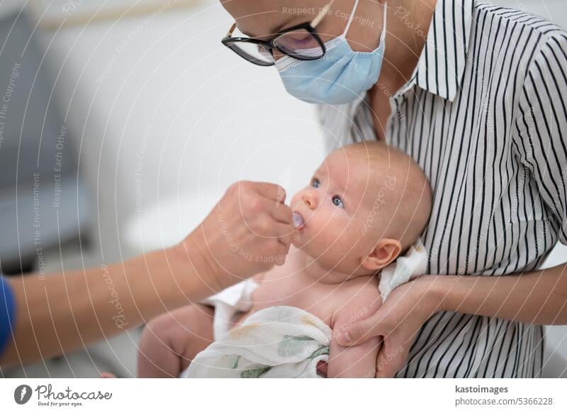 Kinderarzt bei der Verabreichung einer Schluckimpfung gegen die Rotavirus-Infektion an ein kleines Baby im Beisein seiner Mutter. Gesundheitsfürsorge und Krankheitsvorbeugung für Kinder