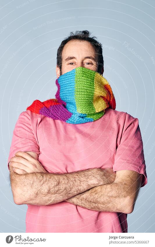 vertikales Porträt eines verrückten Mannes, der sein Gesicht mit einem Regenbogenschal bedeckt. lgbt-Konzept Natur hispanisch quir modern Vielfalt weiß