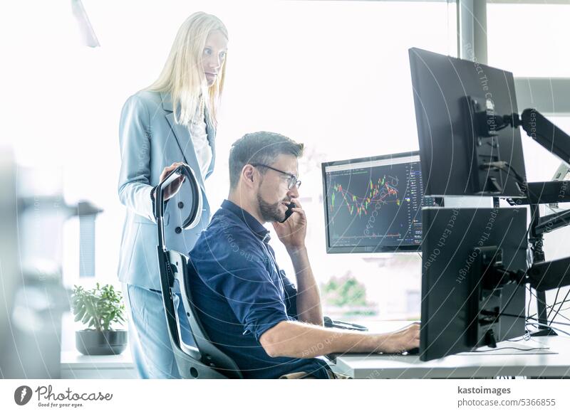 Das Team eines Börsenmaklers, das online handelt, beobachtet Charts und Datenanalysen auf mehreren Computerbildschirmen in einem modernen Büro mit Firmenarbeitsplatz.