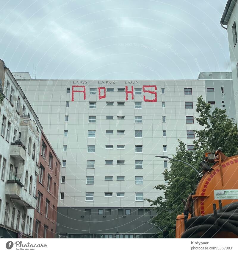 ADHS auf Häuserwand am Kottbusser Tor, Berlin Kreuzberg, davor unten rechts ein orangefarbener Tankwagen Graffitti Kotti Haus Hochhaus rot Farbe tagsüber