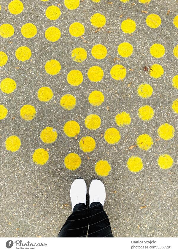 Gelb getupfte Strasse auf dem Vorplatz abstrakt gelb Punkte gelbe Kreise strassenkunst vogelperspektive grau weiße Turnschuhe schwarze hose Betonboden