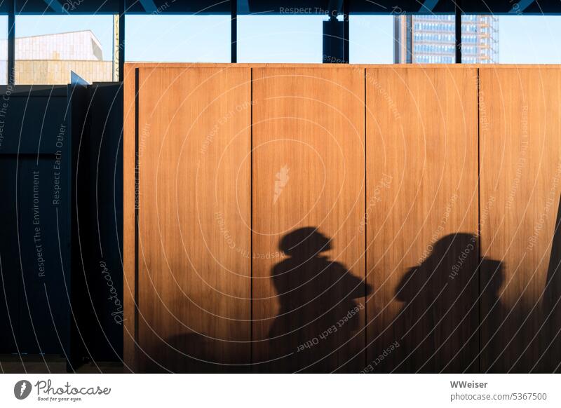 Die Schatten von Ausstellungsbesuchern auf einer sonnenbeschienenen Holzwand Museum Galerie Mann Paar verschränkt nachdenklich betrachten besuchen Besucher