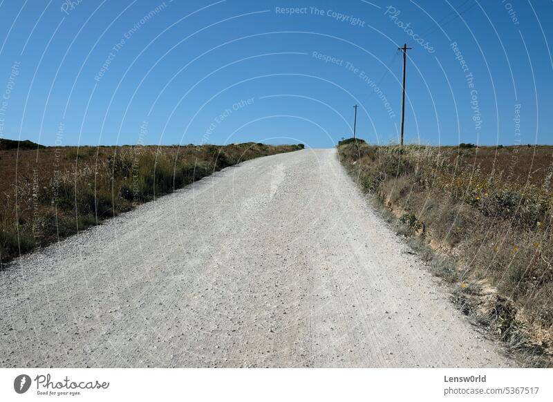 Leere Straße mit einer Stromleitung und einigen Masten daneben in einer ländlichen Gegend in Portugal Landschaft im Freien niemand Horizont Schmutz Weg wüst