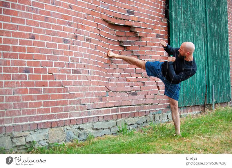 Kampfsportbegeisterter Mann tritt eine Backsteinwand ein eintreten Gewalt Fußtritt Karate Kämpfer Kampfkunst Kick Backsteinfassade kaputt zerstören zerstört