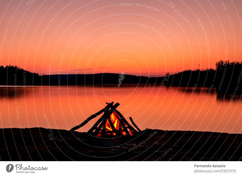 Lagerfeuer. Kleines Lagerfeuer mit sanften Flammen neben einem See während eines glühenden Sonnenuntergangs. San Juan Nacht am Strand. Menschen springen über die Lagerfeuer. Lagerfeuer bei Nacht.