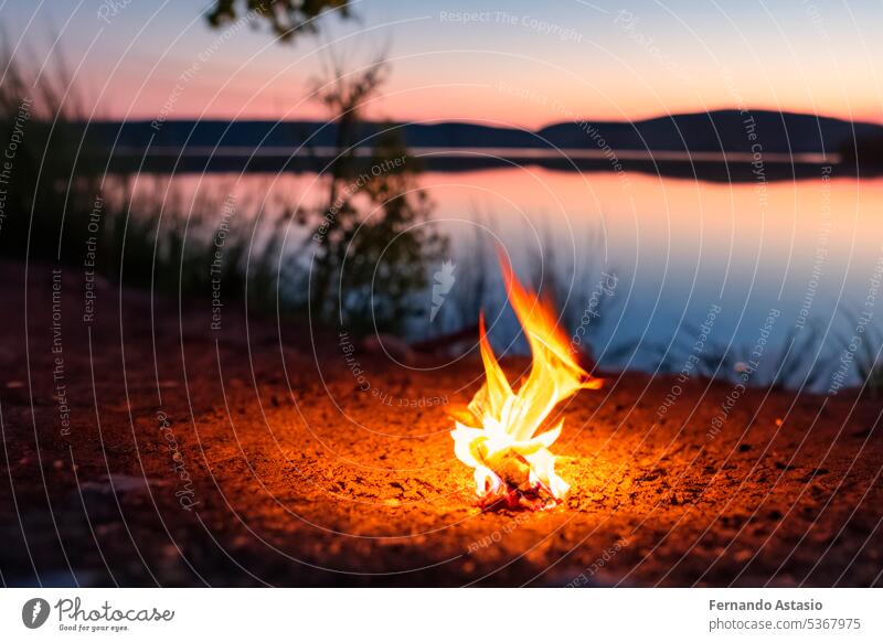 Lagerfeuer. Kleines Lagerfeuer mit sanften Flammen neben einem See während eines glühenden Sonnenuntergangs. San Juan Nacht am Strand. Menschen springen über die Lagerfeuer. Lagerfeuer bei Nacht.