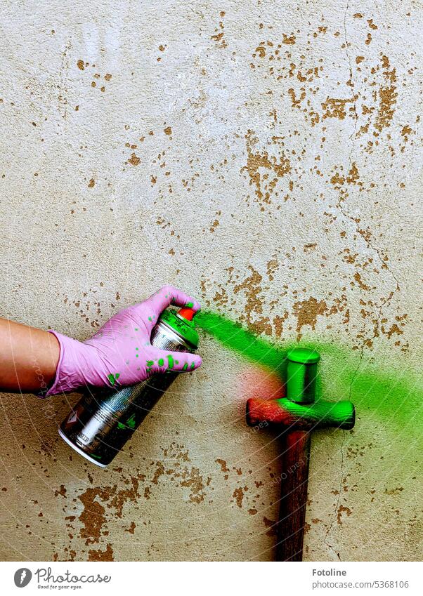 Kunstprojekt! Eine alte Filmdose wird mit grüner Farbe besprüht. Die Hand, die eine Spraydose hält, wird mit einem pinken Einmalhandschuh geschützt. Wand Beton