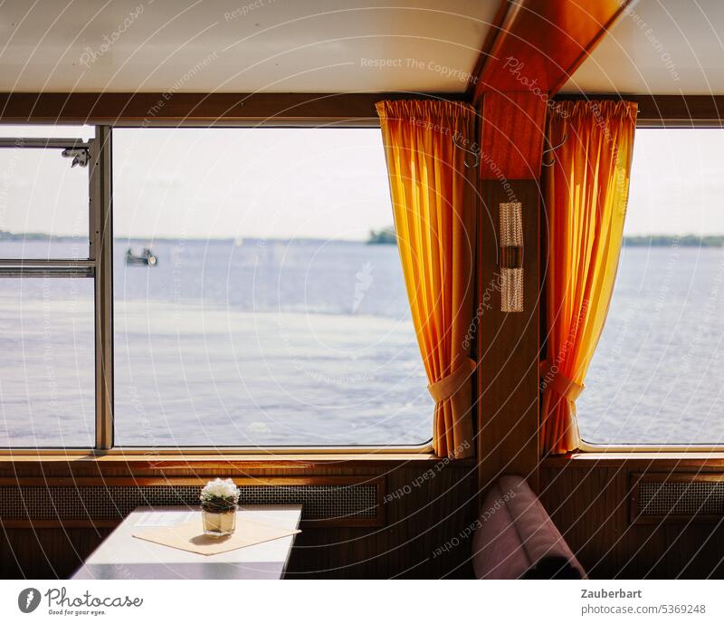 Blick aus dem Fenster eines Passagierschiffs mit orangefarbenen Gardinen auf den See Schiff Fähre Sitzbank Ausblick Freizeit Tisch Gesteck geruhsam Wasser Meer