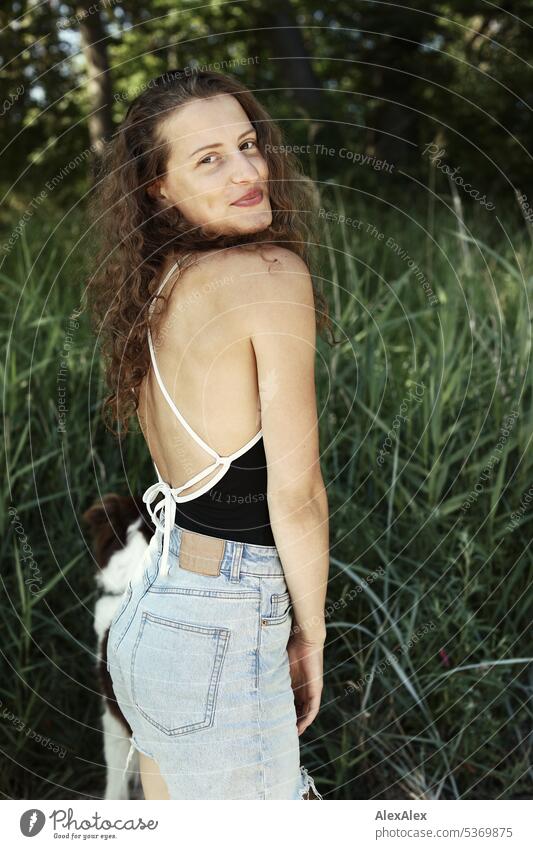 seitliches Portrait einer jungen, schönen, brünetten, lächelnden Frau vor  einem Wald warm sommerlich schönes wetter Sommer Pflanzen Nähe Tag Ruhe Selbstbewußt