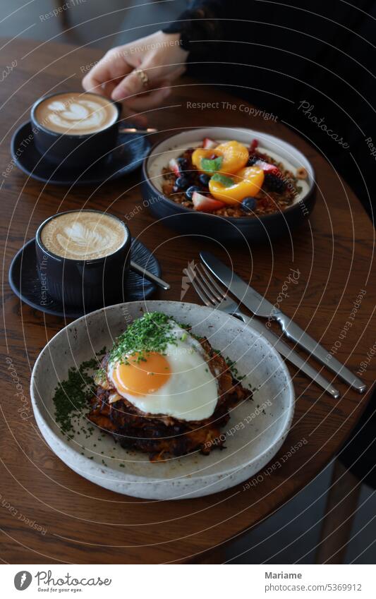 Zwei Tassen Cappucino mit einer Hand, die eine Tasse hält, ein Müsli mit Früchten und Eiern Frühstück Frühstückstisch Brunch Lebensmittel Foodfotografie