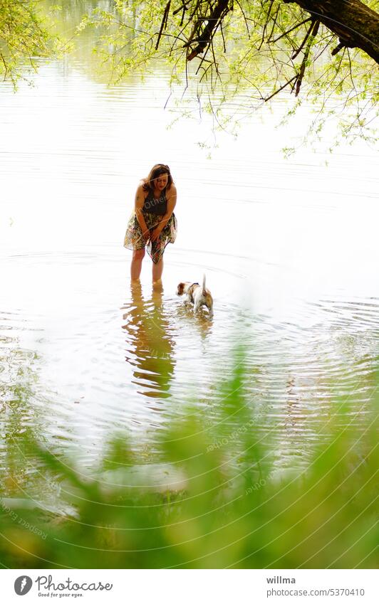 Frau steht mit nackten Beinen im flachen Wasser und spricht mit ihrem Hund Fluss See Ufer baden flaches Wasser Mensch und Tier Sommer Erholung Flussufer Seeufer