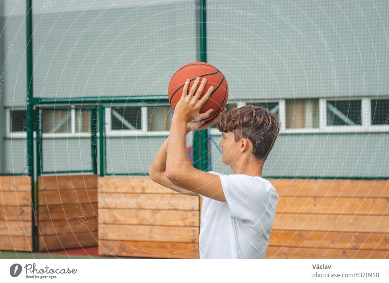 Ein junges Basketballtalent wirft auf seinem Außenplatz Körbe und trainiert für zukünftige Spiele und schwierige Situationen. Er bereitet sich auf die Saison vor. Schießen auf den Korb