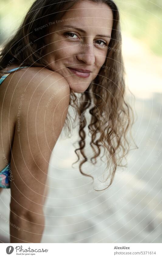 seitliches Portrait einer jungen, schönen, brünetten, lächelnden Frau mit Grübchen im Bikini am Strand warm sommerlich schönes wetter Sommer Nähe Tag
