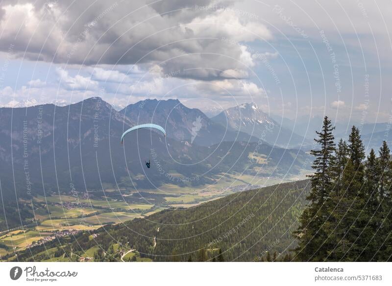 Paraglider schwebt über Berglandschaft Mann Gleitschirm Himmel Gleitschirmfliegen Berge Gebirge Gipfel Wald Landschaft Felder Fichten Wolken Freiheit Alpen