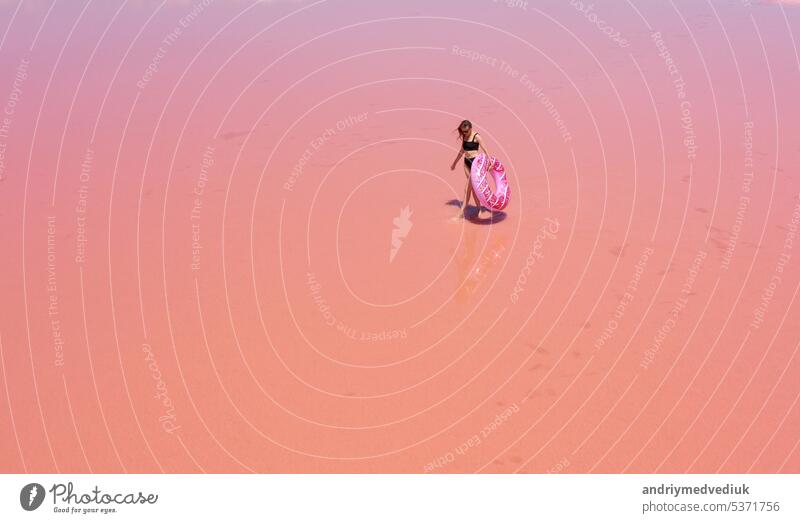 Luftaufnahme. Junge Frau in schwarzem Badeanzug trägt eine aufblasbare rosa Schwimmer in ihren Händen haben Spaß tanzen auf dem rosa Salzsee. Konzept Sommerfestivals, Urlaub, Reise Urlaub, Freiheit, Sonne, genießen
