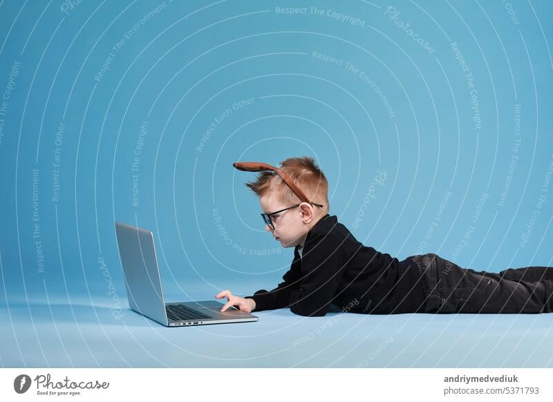 Fernunterricht online Bildung. Schuljunge in Kaninchen Hasenohren auf dem Kopf Studium zu Hause mit Laptop und tun Schule Hausaufgaben auf blauem Hintergrund