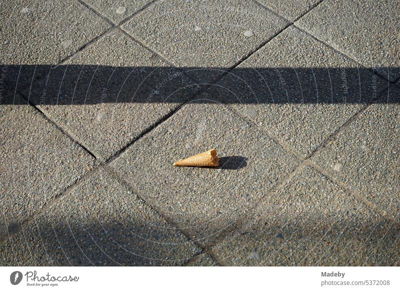 Reste der Waffel einer leeren angebissenen Eistüte auf grauem Straßenpflaster im Frühling bei Sonnenschein in der Altstadt von Detmold in Ostwestfalen-Lippe
