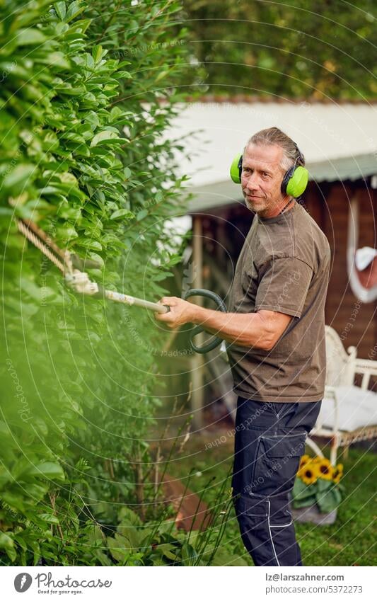 Gärtner beim Schneiden einer Hecke mit einer Heckenschere im Garten eines Kunden, der zum Schutz einen Gehörschutz trägt Kunsthandwerker digital außerhalb