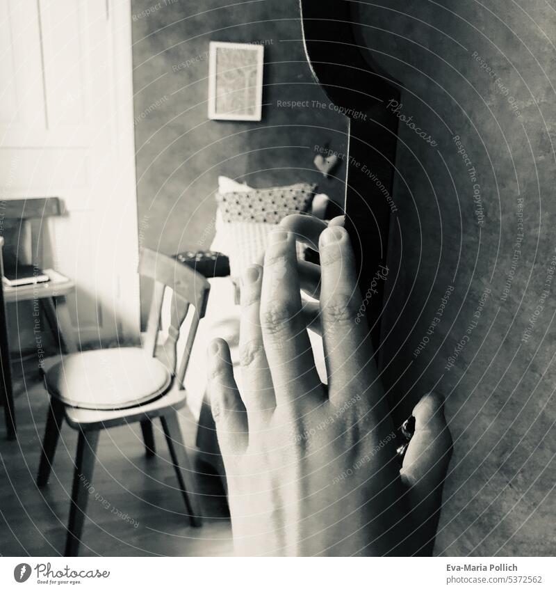 eine Hand an einem Spiegel, im Spiegel ist ein verlassenes Zimmer mit Stuhl und Bett in grau leer reflektieren Licht weiß Raum niemand Schlafzimmer Innenbereich