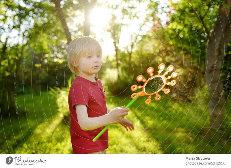 Süßer kleiner Junge spielt mit großen Seifenblasen im Freien. Kind bläst große und kleine Blasen gleichzeitig. Sommer-Freizeit für Kinder. spielen Spaß