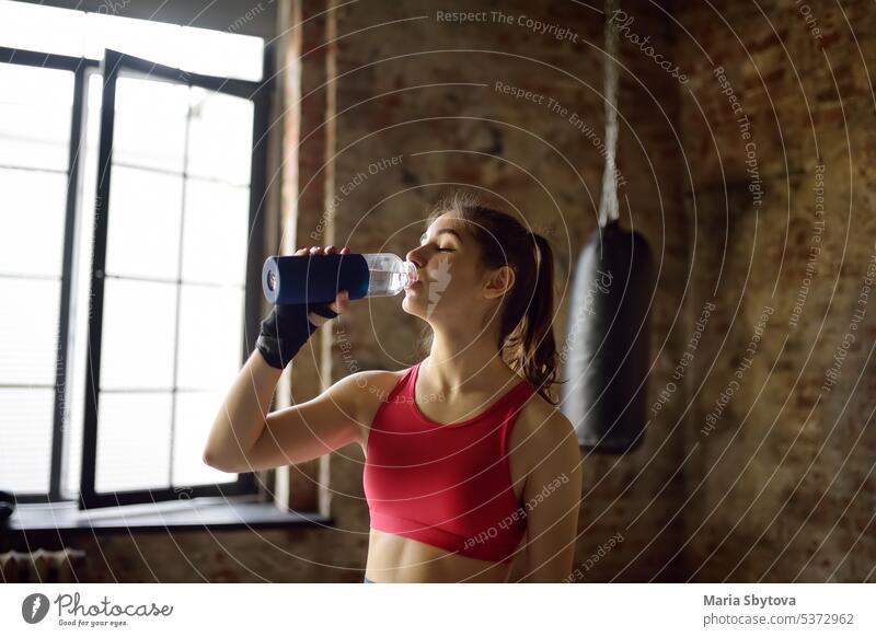 Porträt einer jungen, schönen Sportlerin in einer Boxhalle. Ein Boxer Mädchen trinken Getränk aus einer Flasche während eines Trainings. In den Prozess der Ausbildung brauchen, um eine Menge Wasser zu trinken.