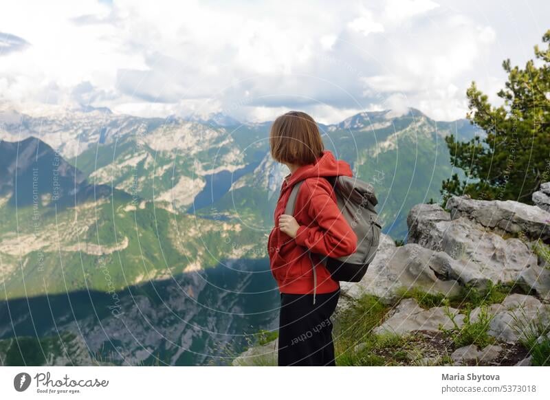 Seitenansicht einer Wanderin, die während einer Wanderung auf einem steinigen Hang eines Bergtals steht. Junge Frau genießt malerische Landschaft mit felsigen Gipfeln beim Trekking in den Alpen